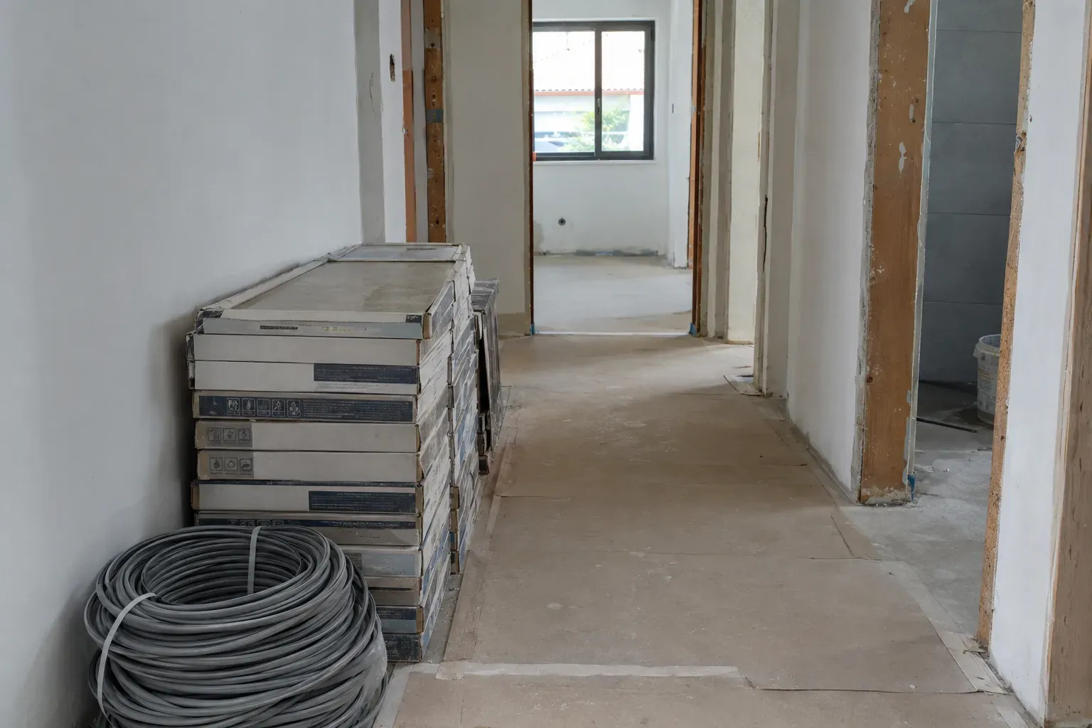 Caixas de azulejos e um rolo de cabo num corredor de casa em obra.