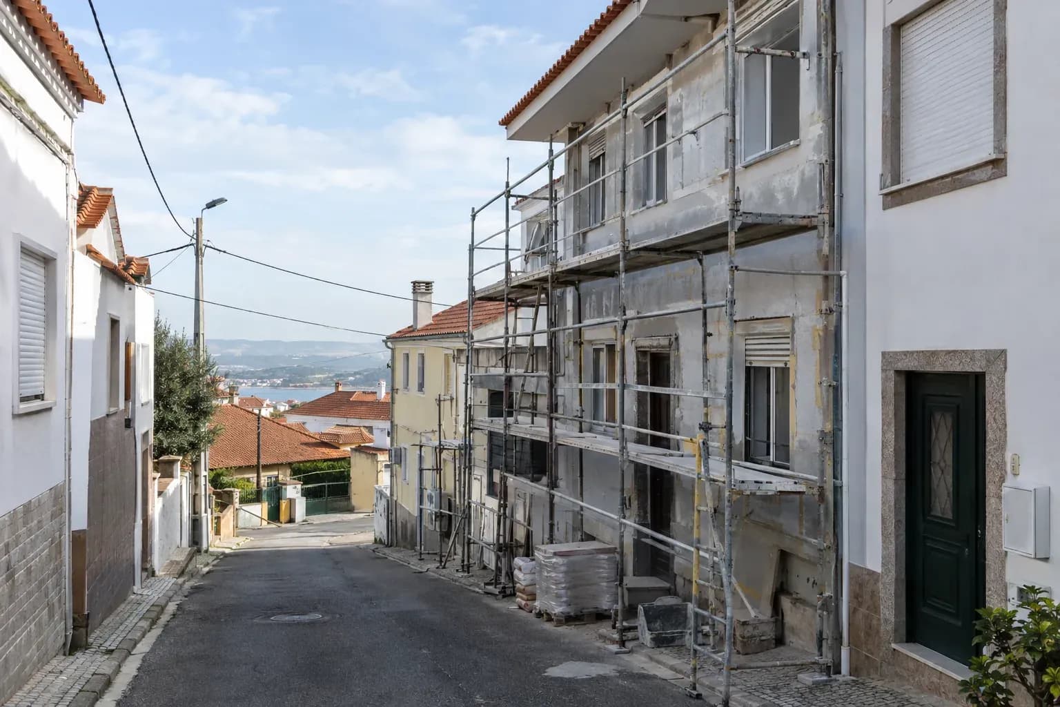 Rua residencial de uma vila portuguesa, com um prédio em obra e andaimes.