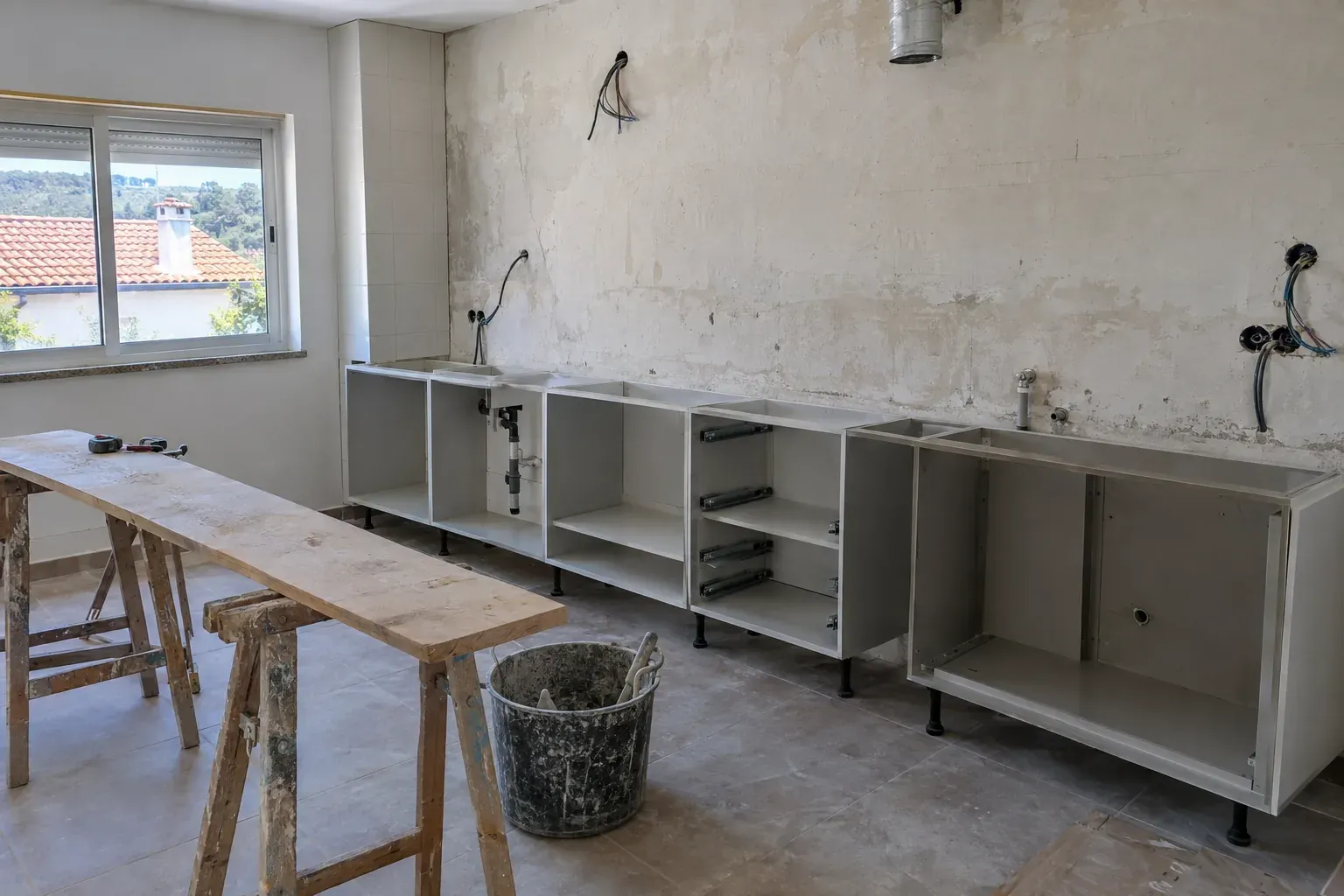 Cozinha em obra, com módulos de armários sem portas e uma parede com canalizações à vista.